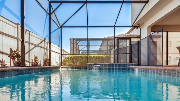 A swimming pool with a glass enclosure, surrounded by a white wall and a metal fence. - Luxurious Vacation Home With Private Pool!!! (Kissimmee)