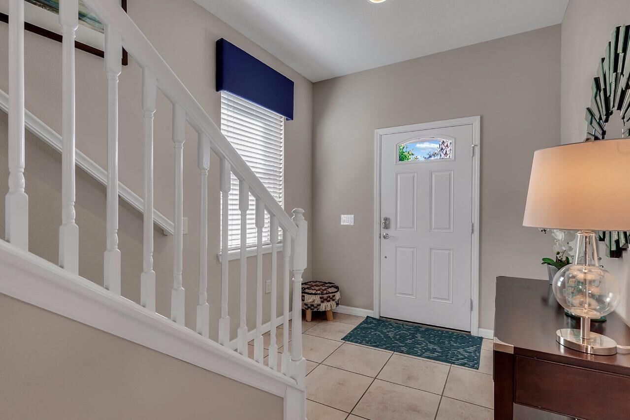 A hallway with a white staircase, a door with a stained glass window, and a lamp on a table.