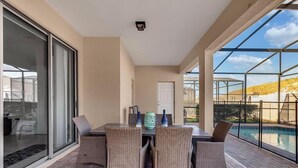 A patio with a table and chairs, a pool, and a glass door leading to a covered area. - Luxurious Vacation Home With Private Pool!!! (Kissimmee)