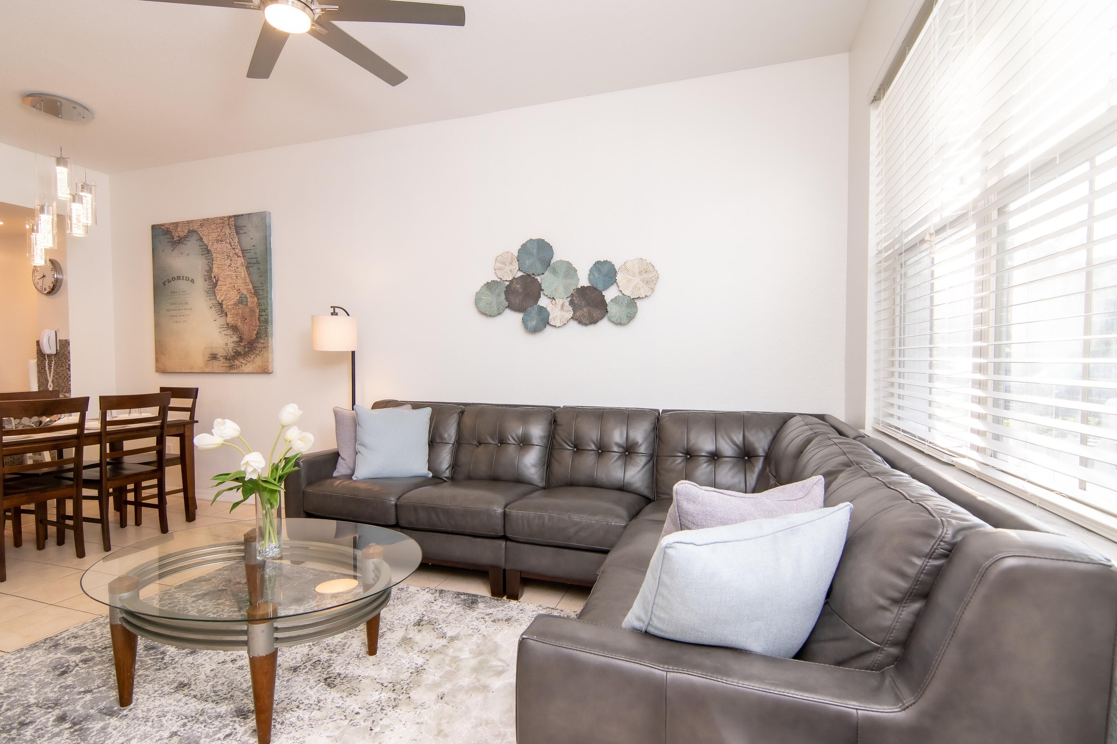 A modern living room with a leather sofa, glass coffee table, and a decorative wall piece.