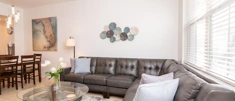 Uma sala de estar moderna com sofá de couro, mesa de centro de vidro e um objeto decorativo na parede.