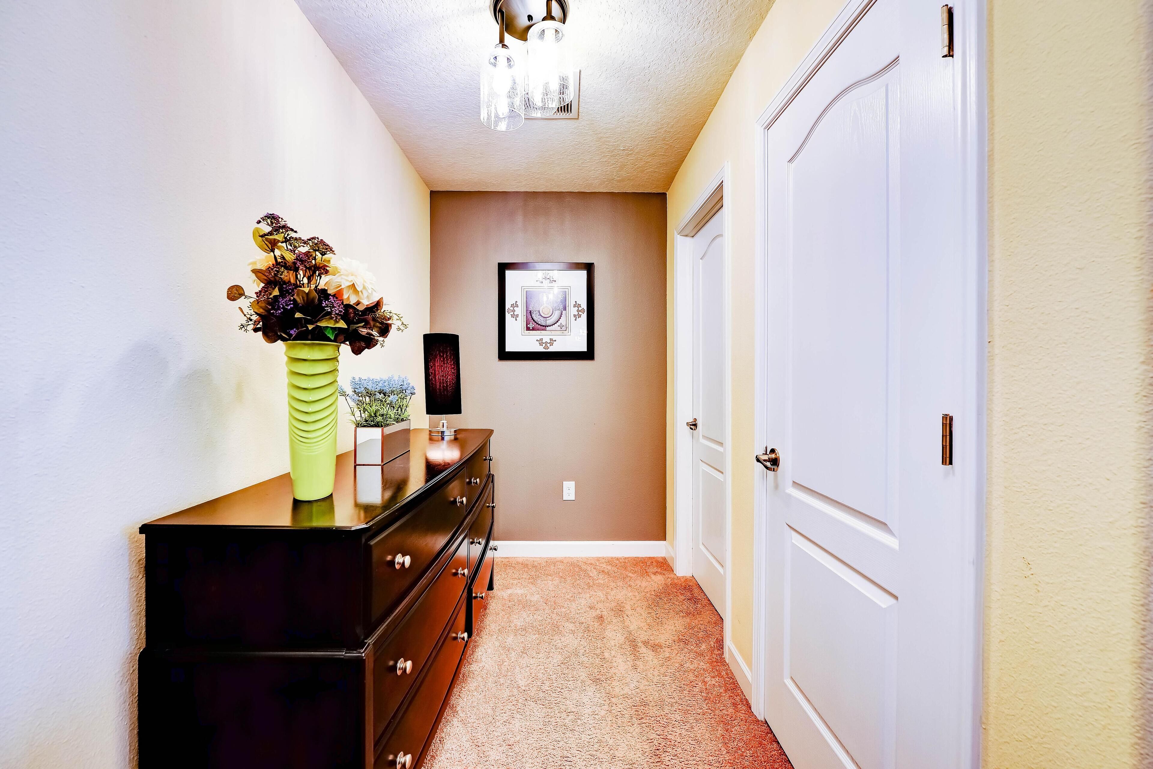A hallway with a dresser, a vase of flowers, a framed picture on the wall, and a door.