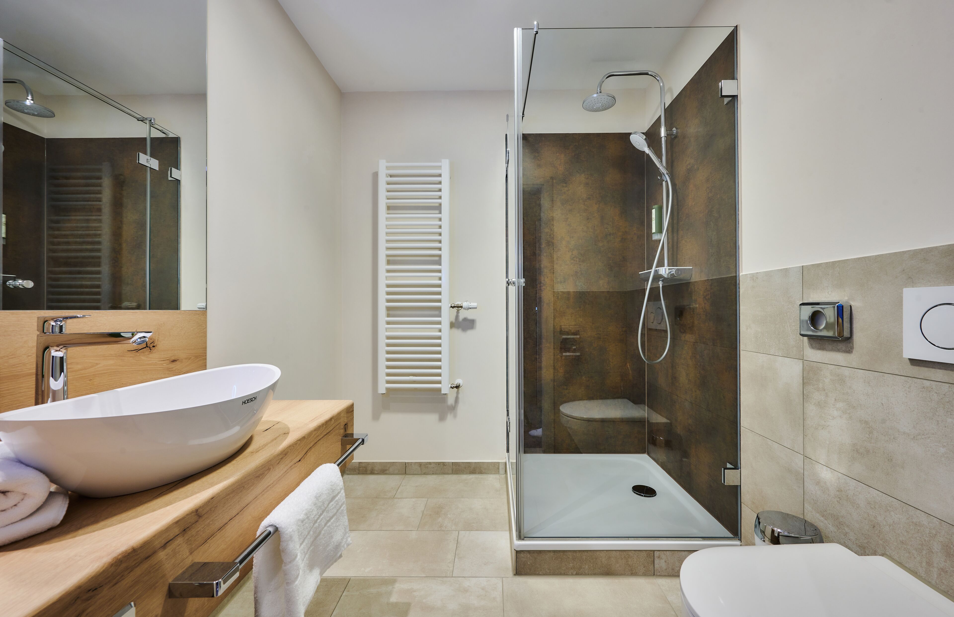 Un baño moderno con ducha de vidrio, un lavamanos grande y blanco, y un inodoro.