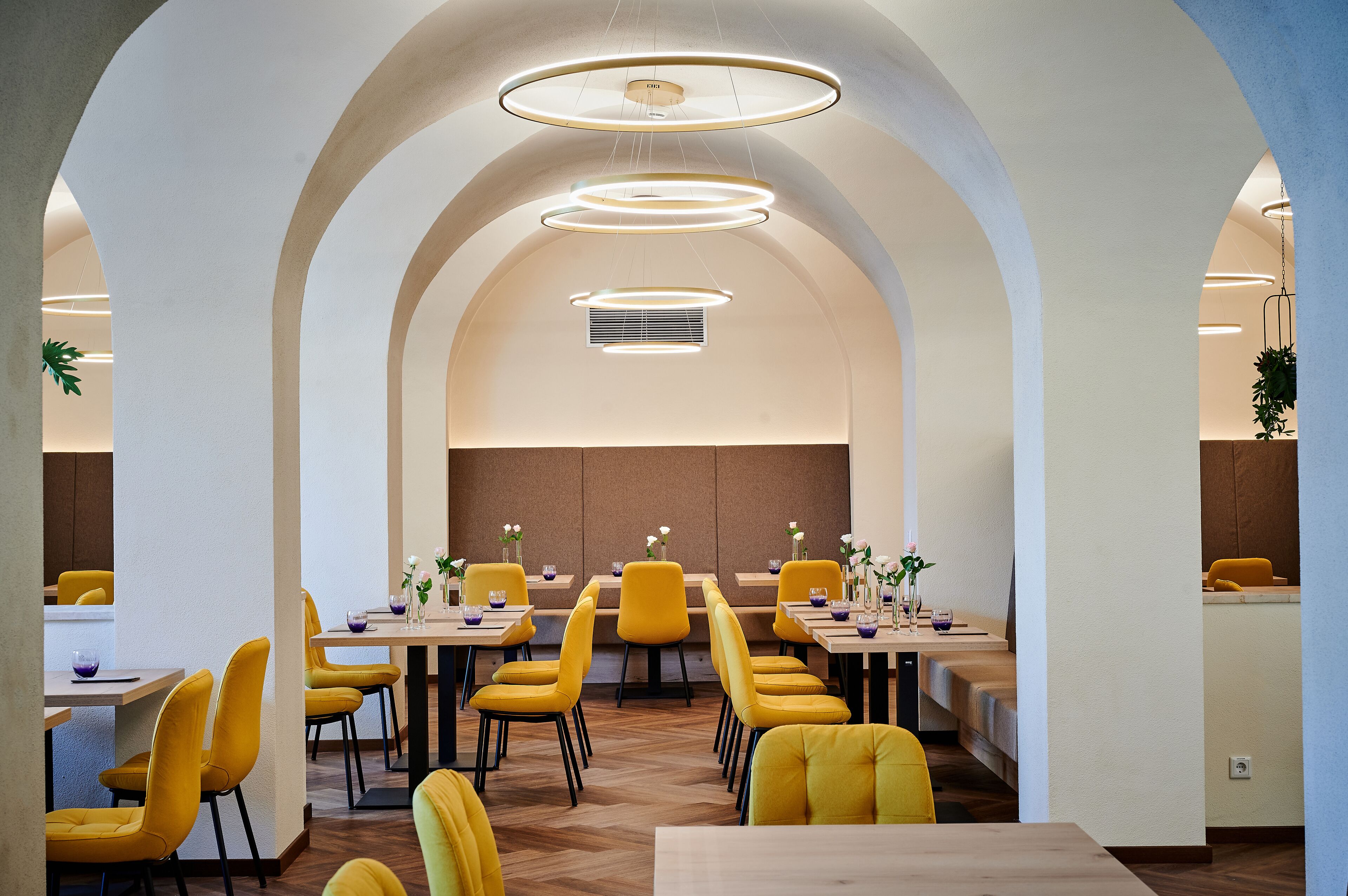 Uma sala de jantar moderna com cadeiras e mesas amarelas, tetos em arco e iluminação pendente.