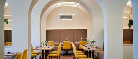 A modern dining area with yellow chairs and tables, arched ceilings, and pendant lighting.