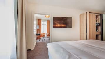 A hotel room with a large bed, a TV mounted on the wall, a wooden wardrobe, and a desk with a chair.