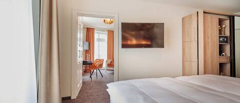 A hotel room with a large bed, a TV mounted on the wall, a wooden wardrobe, and a desk with a chair.