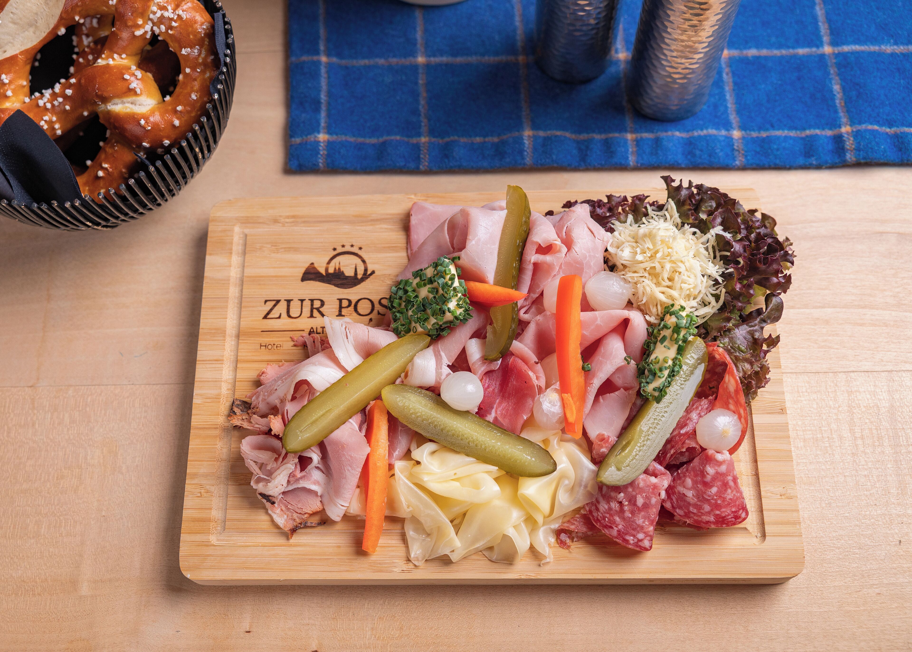 A wooden board with various meats, cheeses, and vegetables, likely a charcuterie board.