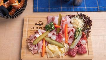 A wooden board with various meats, cheeses, and vegetables, likely a charcuterie board.