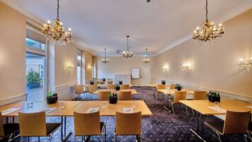 A conference room with multiple tables, chairs, and chandeliers.