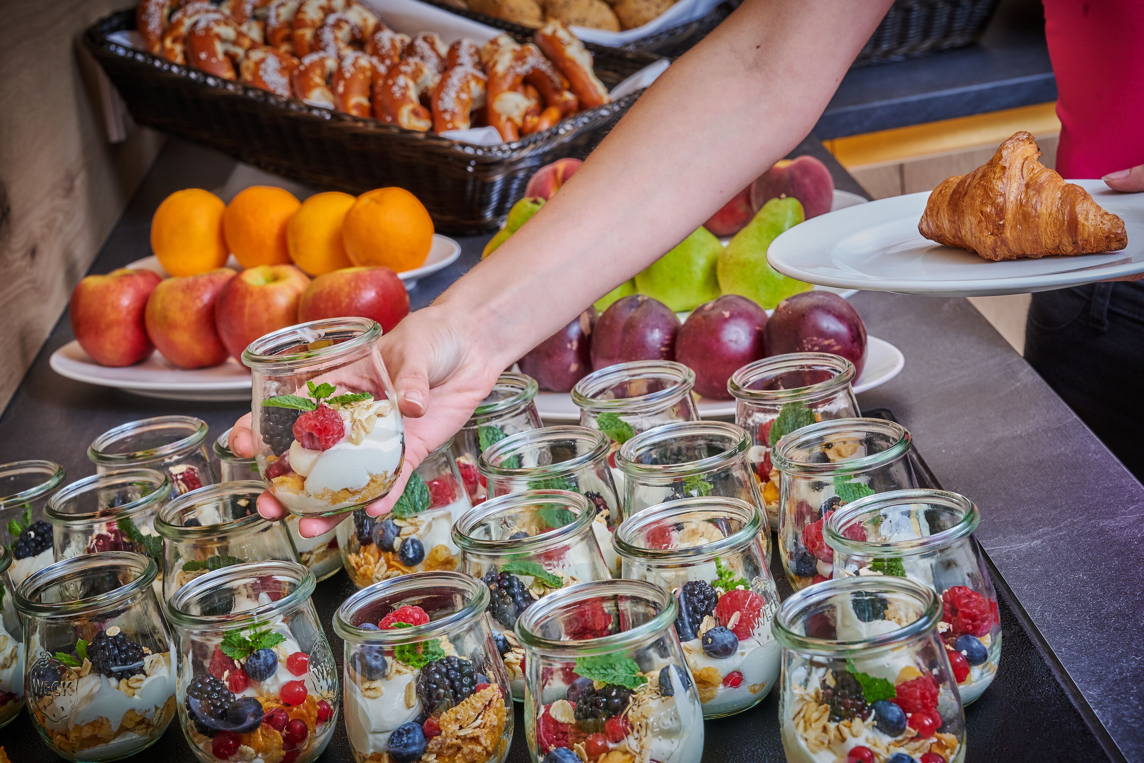 A buffet with various food items including fruits, pastries, and a croissant.