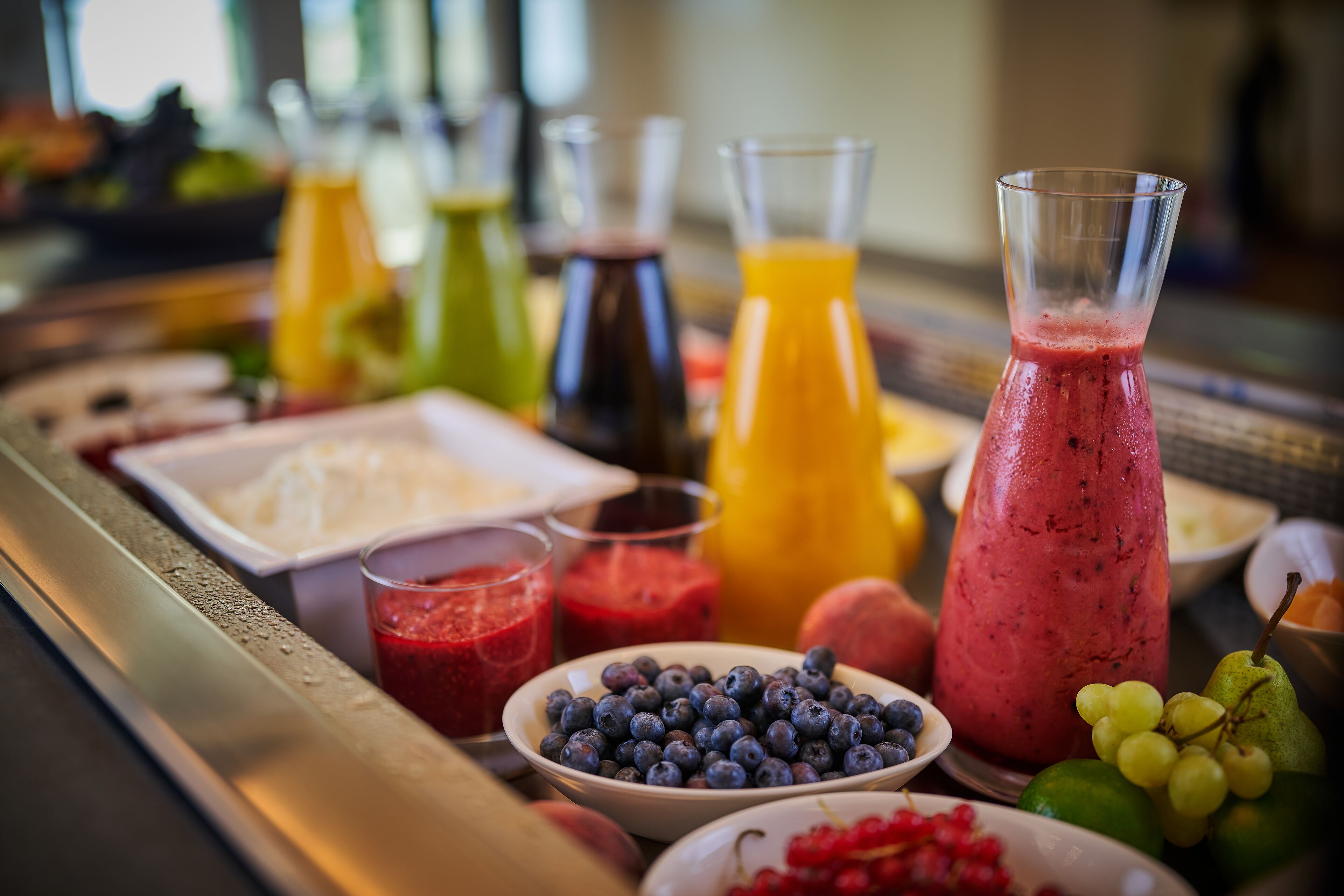 Un buffet de petit-déjeuner proposant une variété de fruits, des jus de fruits et un grand pichet rempli de smoothie.