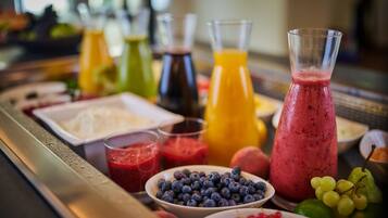 A breakfast buffet with various fruits, juices, and a large pitcher of smoothie.