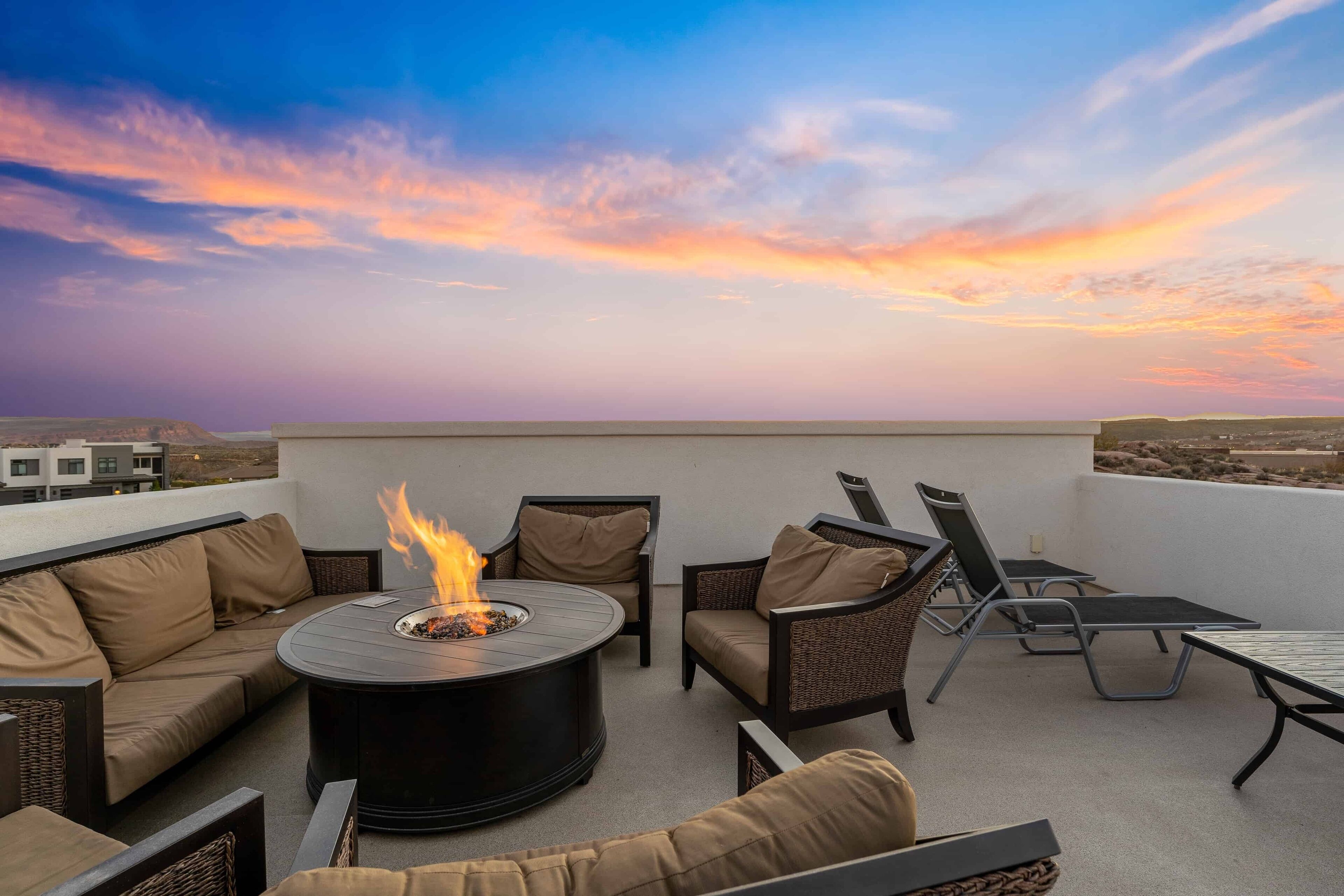 A rooftop terrace with a circular fire pit, seating area, and a view of the cityscape during sunset.