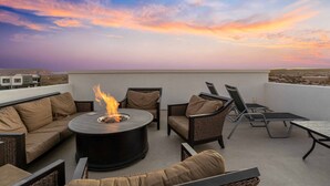 A rooftop terrace with a circular fire pit, seating area, and a view of the cityscape during sunset.