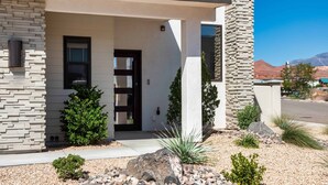 A modern house with a stone facade, a black door, and a small garden with rocks and plants.