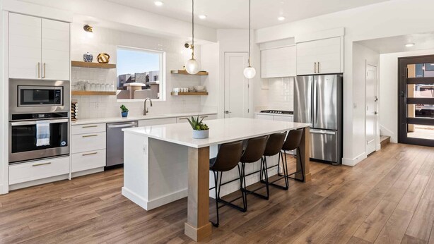 A modern kitchen with white cabinetry, stainless steel appliances, a central island with bar stools, and pendant lighting.