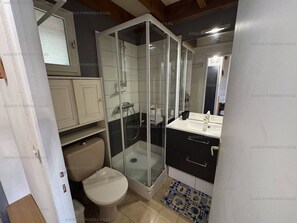 Un baño pequeño con ducha compartimentada por vidrio, inodoro y lavamanos con espejo.