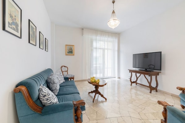 Una sala de estar con un sofá, un televisor, una mesa con flores y cuadros en la pared.