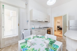 Cocina compacta con lavadora, lavaplatos y comedor con mesa dispuesta para cuatro.