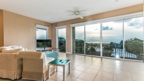 A spacious living room with a large sliding glass door leading to a balcony, a ceiling fan, and a flat-screen TV.