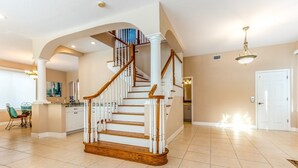 A spacious living area with a wooden staircase, a dining area, and a kitchen.