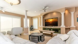 A spacious living room with a large sectional sofa, a round coffee table, and a flat-screen TV mounted on a fireplace wall.