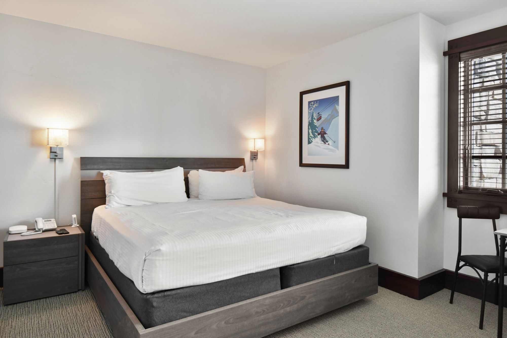 Moderni hotellihuone, jossa on suuri sänky, yöpöytävalaisimet, puhelin ja seinällä oleva kehystetty taulu.