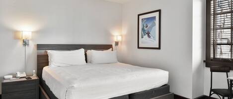 Moderni hotellihuone, jossa on suuri sänky, yöpöytävalaisimet, puhelin ja seinällä oleva kehystetty taulu.