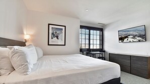 A modern hotel room with a large bed, a desk, and a window with blinds. - Deer Valley Ski Condo with Parking (Park City)
