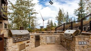 An outdoor kitchen with stone walls, two grills, a sink, and a small covered seating area. - Ski-In Ski-Out Condo at Deer Valley (Park City)