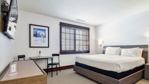 A hotel room with a bed, a desk, two chairs, a window with blinds, and a framed picture on the wall. - Ski-In Ski-Out Condo at Deer Valley (Park City)