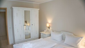 Une chambre d’hôtel avec une grande armoire blanche, une table de chevet avec une lampe et deux lits avec du linge de lit blanc.