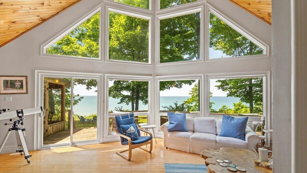 Une pièce spacieuse dotée de grandes fenêtres offrant une vue sur l’océan, d’un plafond en bois et d’un coin salon confortable avec un canapé et des fauteuils.