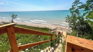 Un escalier en bois mène à une plage bordée d’une eau d’un bleu limpide.