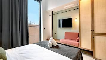 Una habitación de hotel con cama, televisor montado en la pared, sofá y armario.