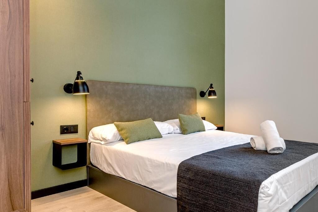 Habitación de hotel con cama, lámparas de noche, mesita de noche y una toalla enrollada.