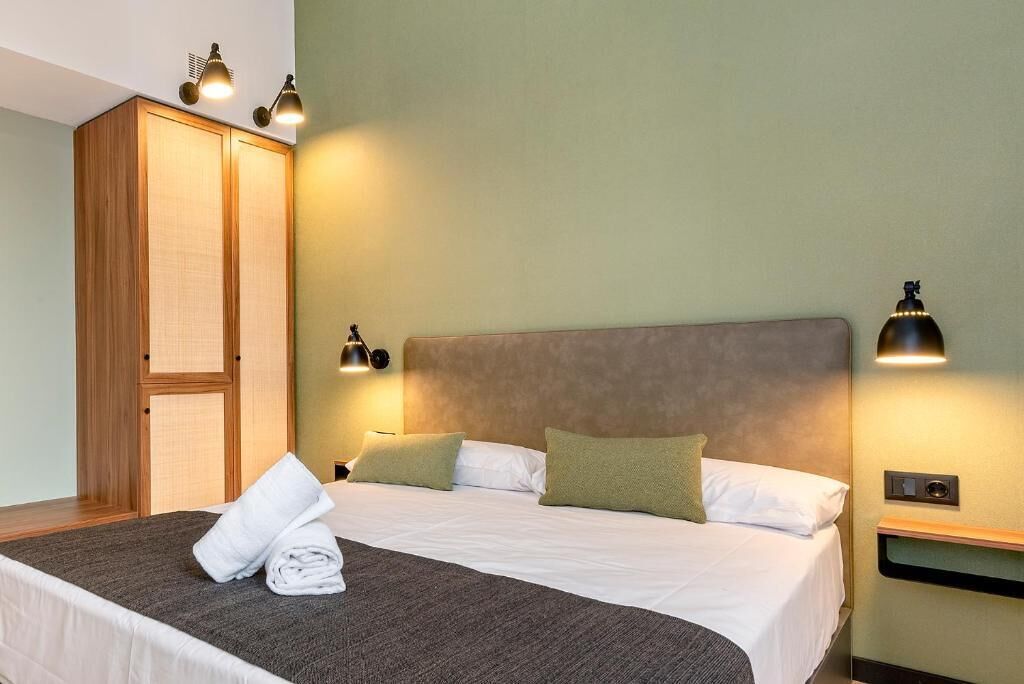 A hotel room with a bed, two bedside lamps, a wardrobe, and a nightstand.