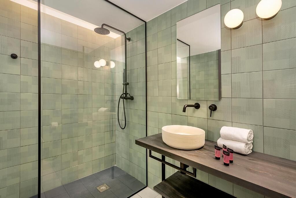 A modern bathroom with a glass-enclosed shower, a round sink, and a mirror with two wall-mounted lights.