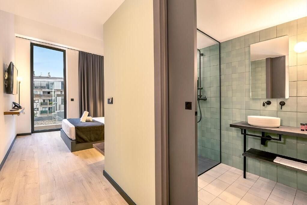 A modern hotel room with a balcony, a separate bathroom with a glass shower, and a large mirror.