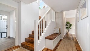 Una escalera moderna con peldaños de madera y barandillas blancas, que conduce a un rellano con un banco y una planta en maceta.