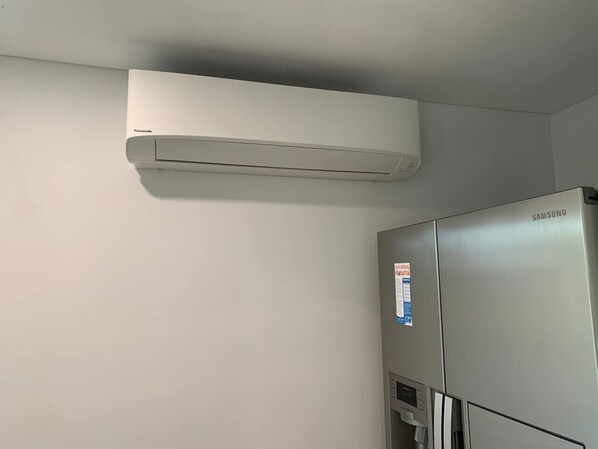 Un réfrigérateur Samsung dans une cuisine, avec un climatiseur Panasonic fixé au mur.
