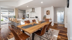 Una cocina moderna con armarios blancos, una isla central y un comedor con mesa y sillas de madera.
