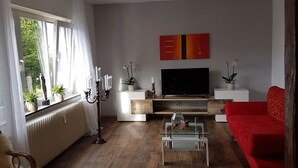 A living room with a TV, red sofa, and potted plants. - Vacation apartment in Wermelskirchen, Bergisches Land, near Cologne and Düsseldorf (Wermelskirchen)