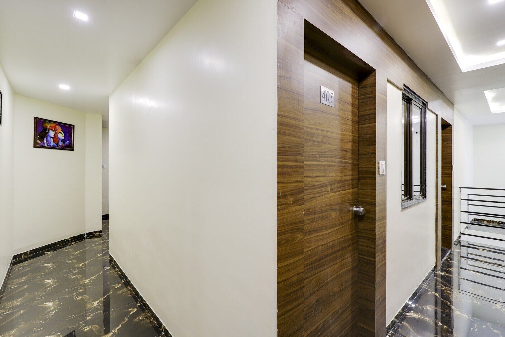 Un pasillo con puerta de madera marcada con el número 405, suelo de mármol y un ventanal pequeño.