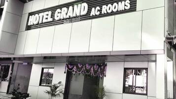 A building with a sign reading "HOTEL GRAND AC ROOMS".