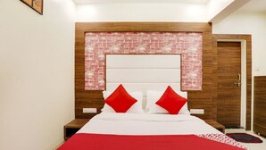 Un dormitorio con cabecera de ladrillo, cama con ropa de cama blanca y almohadas rojas, y un armario de madera.