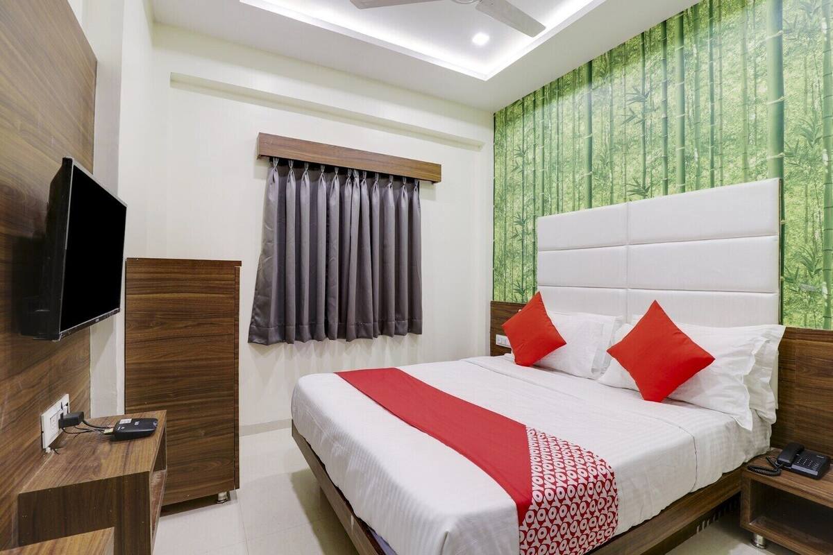 Habitación de hotel con cama, televisor, escritorio y ventana con cortinas.