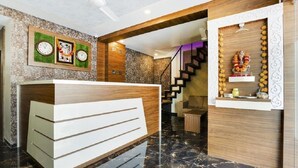 Zona de recepción con mostrador, escalera y un reloj en la pared.