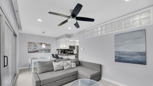 Ein modernes Wohnzimmer mit einem grauen Ecksofa, einem Glastisch, einem Deckenventilator und einem großen abstrakten Gemälde an der Wand.